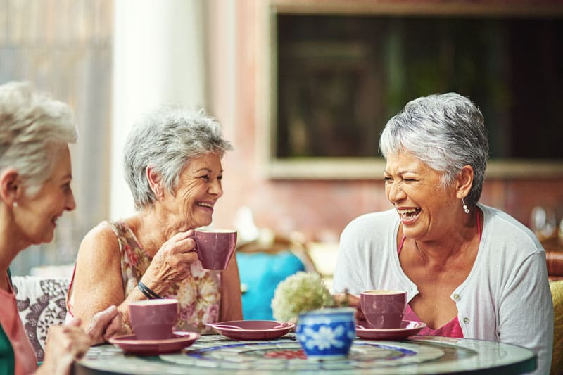 Three seniors laughing while drinking hot beverages