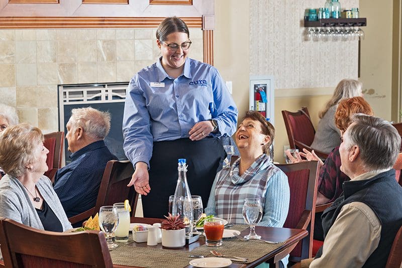 Server laughing with senior residents in dining room